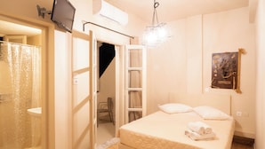 A bedroom with a bed, a TV, and a shower area. - Villa Toula (Santorini)