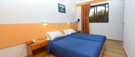 A bedroom with a double bed, a nightstand with a phone, a wall-mounted light, a window with curtains, and a painting on the wall.