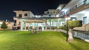 Un hôtel doté d’un espace extérieur couvert avec des sièges, d’une pelouse bien entretenue et d’une enseigne indiquant « HÔTEL ET APPARTEMENTS ANIXIS ».