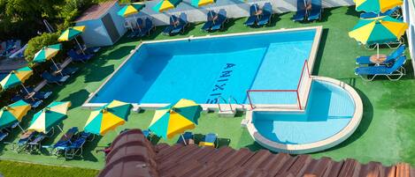 A swimming pool with multiple sun loungers and umbrellas, surrounded by green artificial turf.