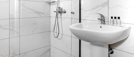Un baño moderno con cabina de ducha de vidrio, lavamanos blanco y azulejos de mármol.
