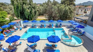 Un espace piscine agrémenté de plusieurs parasols bleus, de chaises longues et offrant une vue dégagée sur le paysage environnant.