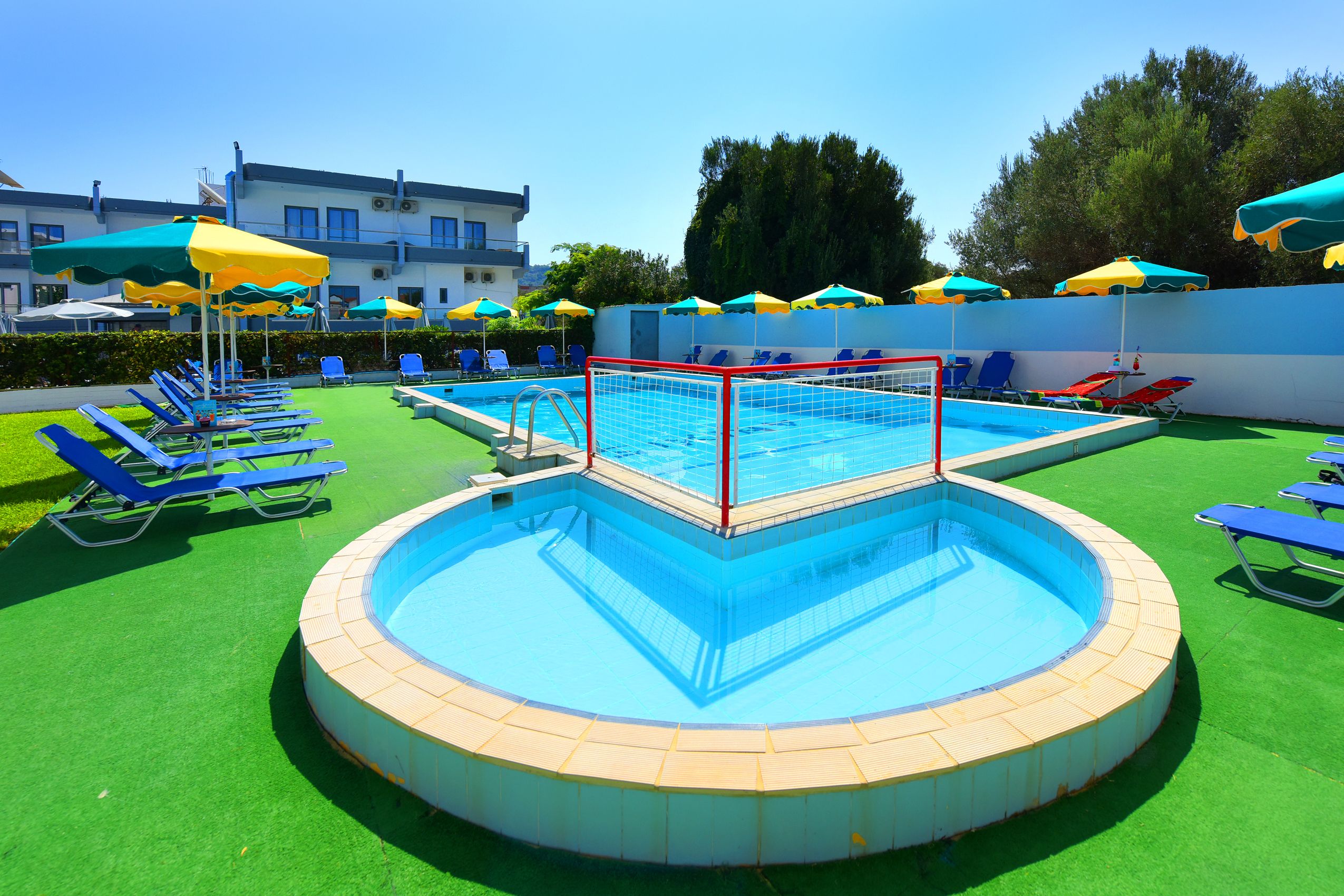 Zona de piscina con piscina circular, sillas reclinables azules y sombrillas.
