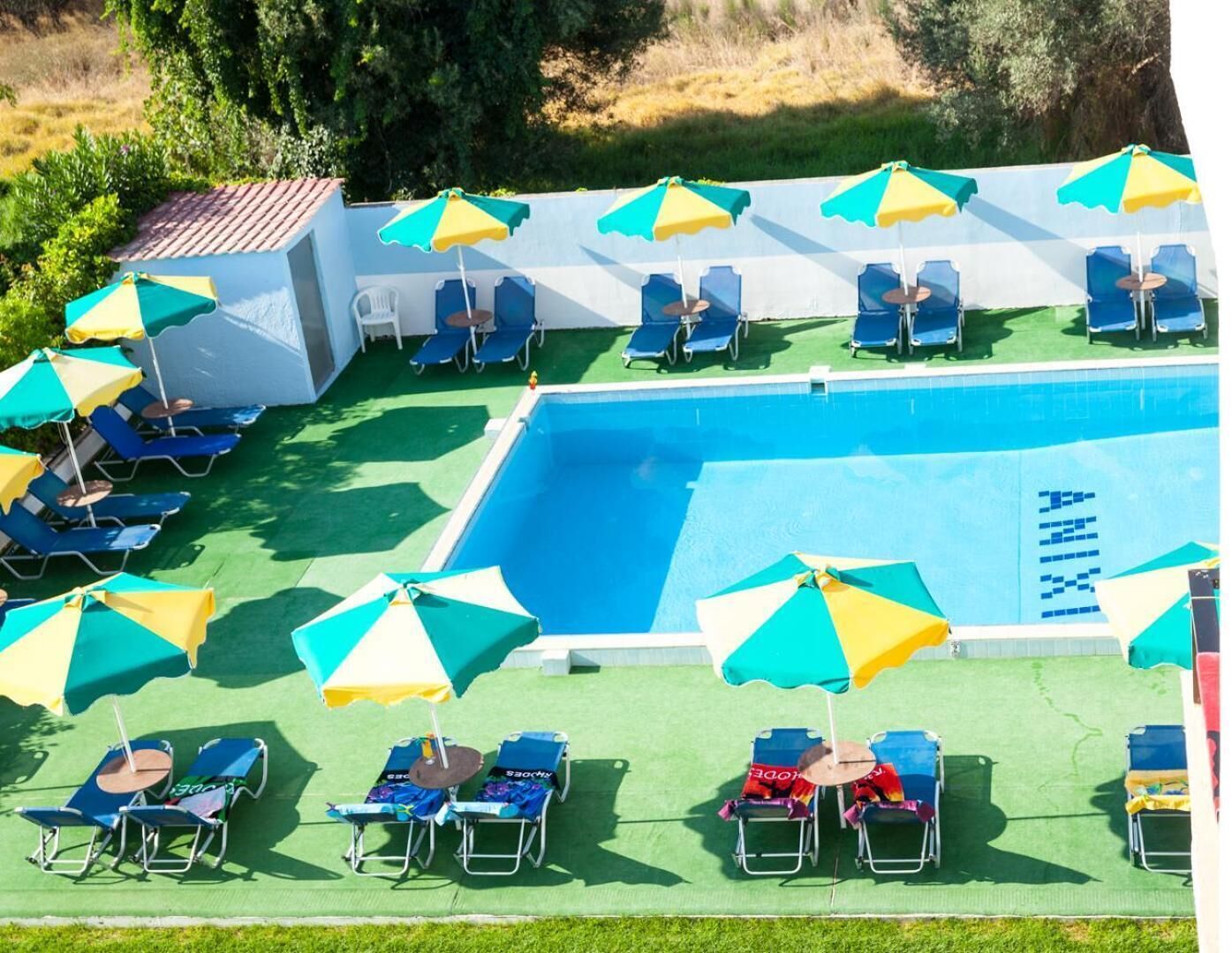 Une piscine entourée de nombreuses chaises longues et de parasols, elle-même bordée d’une pelouse verdoyante et d’un bâtiment blanc.
