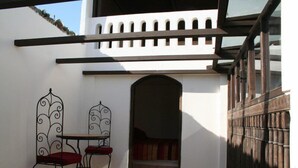 Une terrasse avec deux chaises en métal et une petite table, une porte en arc de cercle et une clôture en bois.