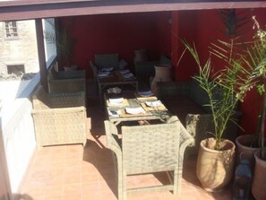 An outdoor patio with wicker furniture, a table with papers, and potted plants. - Riad Dar Nor (Essaouira)