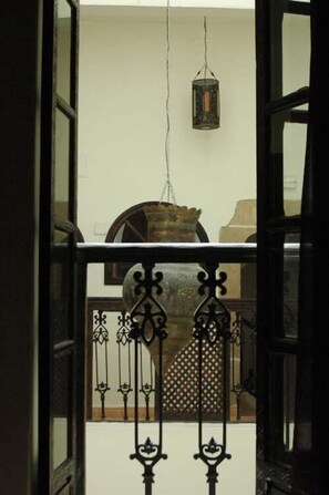 An open door with a wrought iron railing, a hanging lantern, and a rustic wooden chair in the background. - Riad Dar Nor (Essaouira)