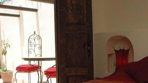 Une chambre avec un grand lit, une porte en bois et une vue sur un balcon agrémenté d’une table et de chaises.