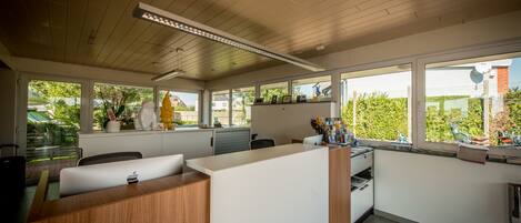 A modern office space with a wooden reception desk, white walls, and large windows offering views of greenery and a brick building.