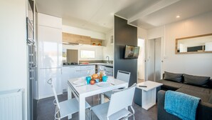 A modern kitchen with white cabinets, a dining table set for two, and a grey sofa in the living area. - Holiday Village Knokke (Knokke-Heist)
