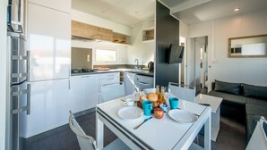 A modern kitchen with white cabinetry, a dining table set with plates, cups, and a fruit bowl. - Holiday Village Knokke (Knokke-Heist)