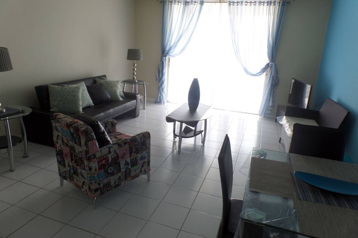 A living room with a sofa, a patterned armchair, a coffee table, a TV, and a lamp.