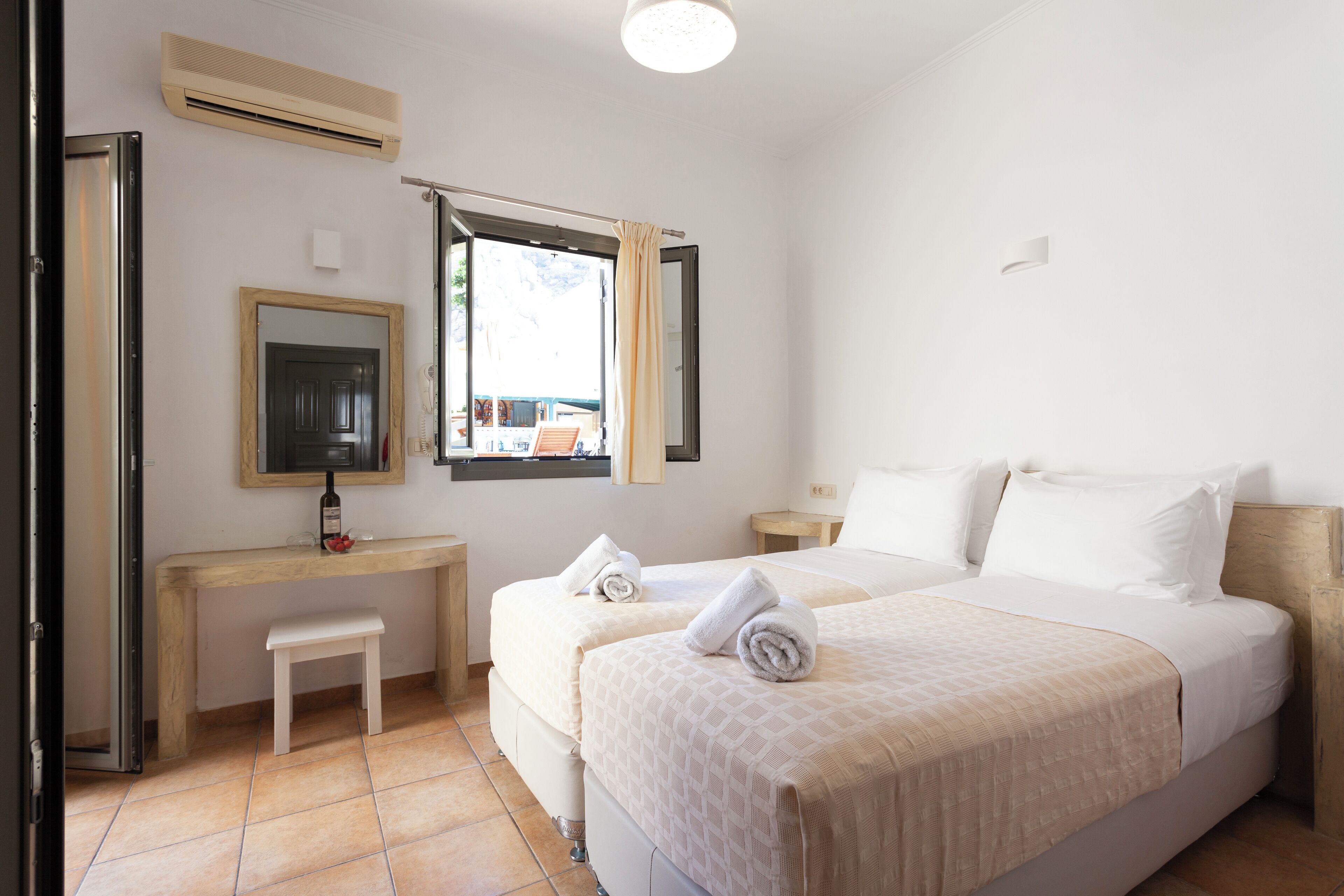 Habitación de hotel con cama, escritorio, silla, espejo y ventana con cortinas.