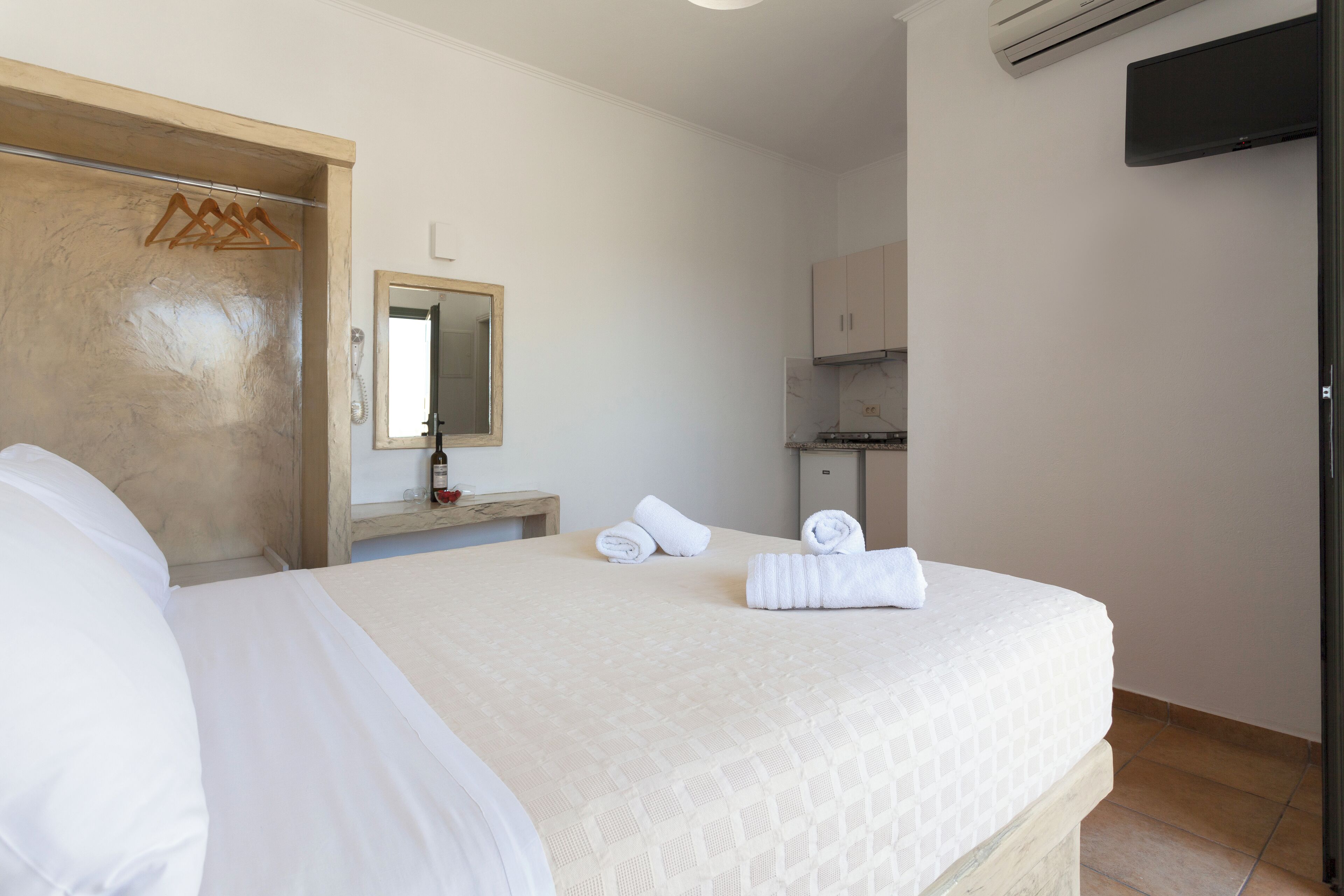 Habitación de hotel con una cama, un armario de madera, un espejo, una mesita con una botella y un televisor montado en la pared.