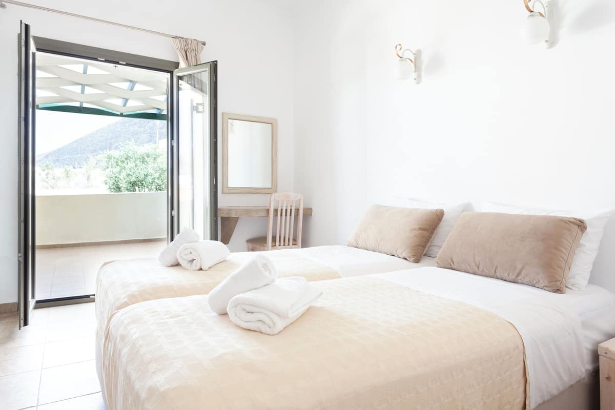 A hotel room with two beds, a large window, a wooden desk, and a mirror.