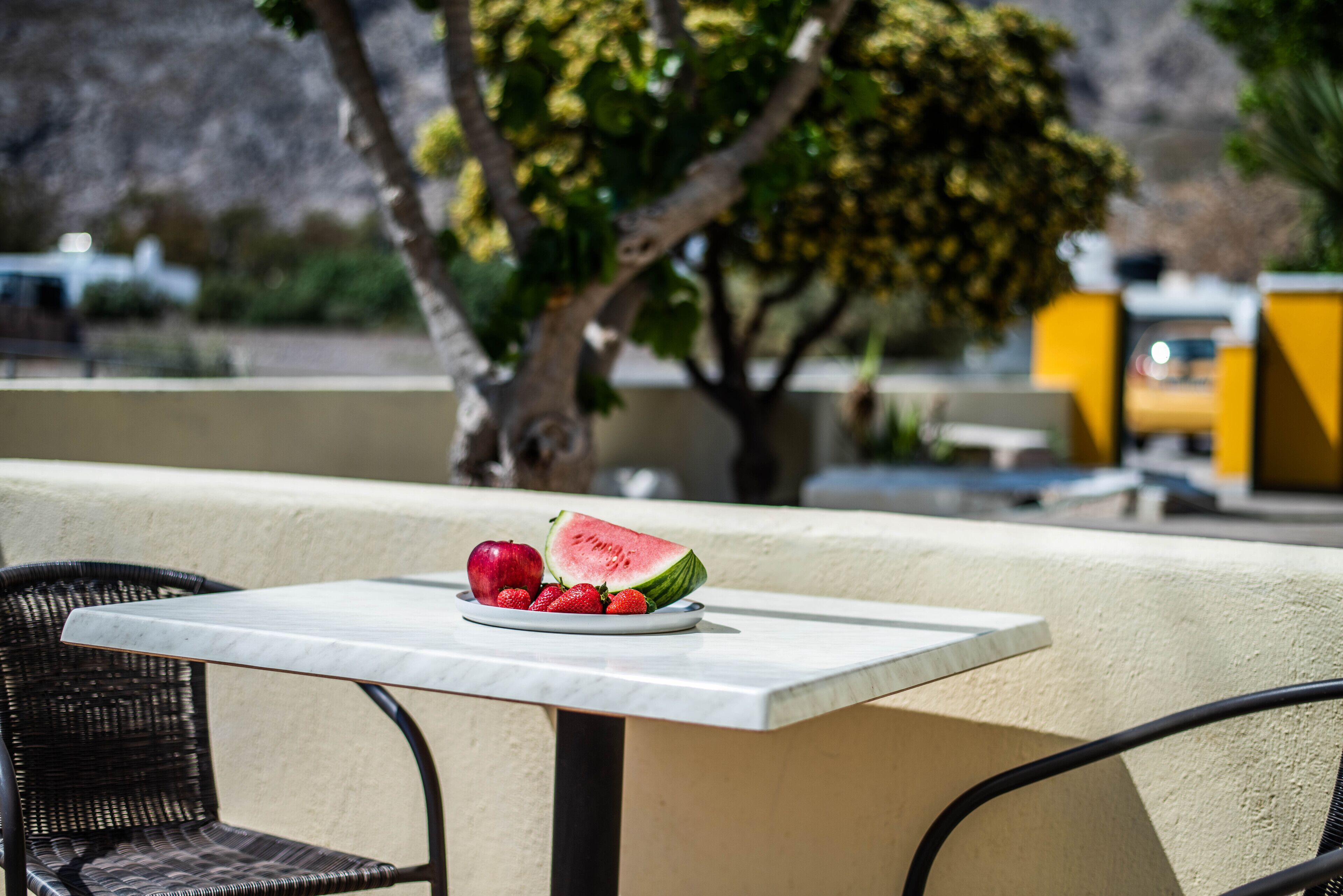 A table with a plate of fruit and a chair.