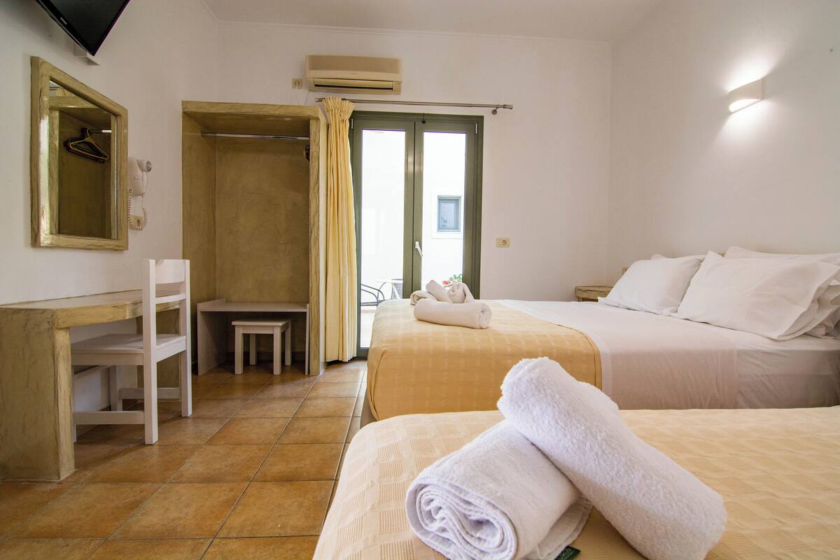 A hotel room with two beds, a desk, a chair, a mirror, and a shower area.