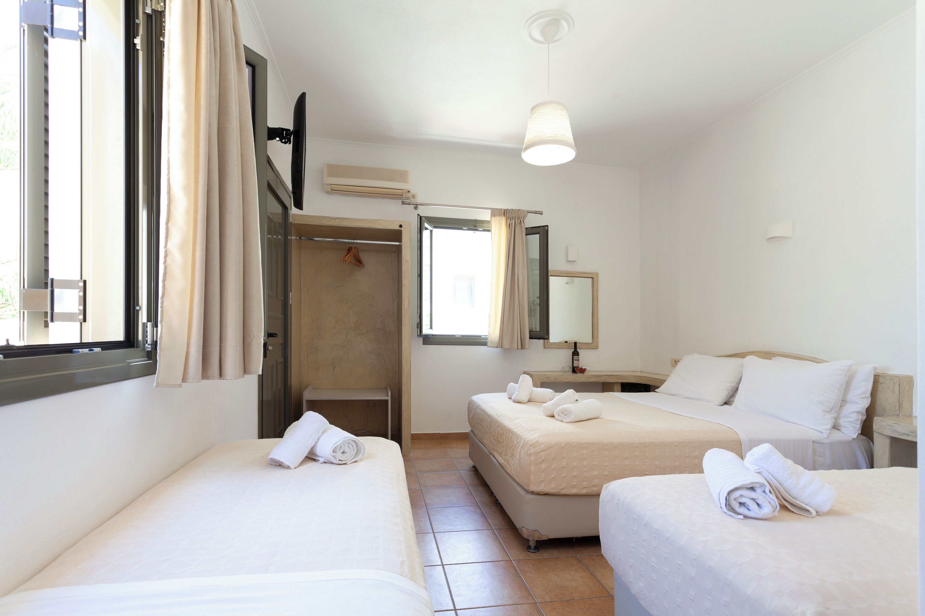 A hotel room with two single beds, a bathroom, a window with curtains, a mirror, and a ceiling light.