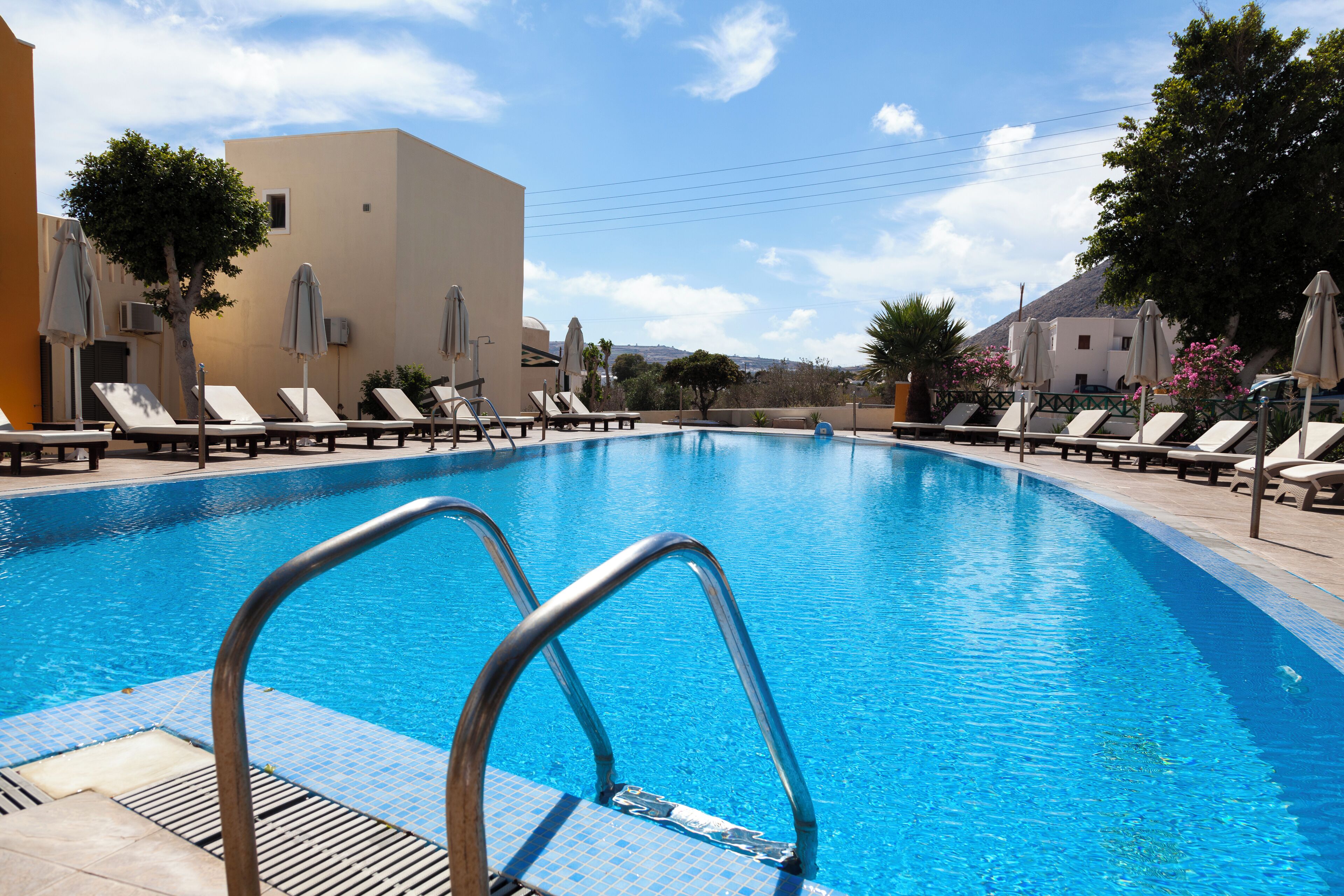 A swimming pool with lounge chairs and umbrellas, surrounded by buildings and trees.