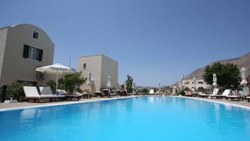 A swimming pool with lounge chairs and umbrellas, surrounded by buildings and a mountain in the background.