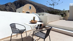 A terrace with two wicker chairs and a table, a fruit bowl, and a view of a mountain.