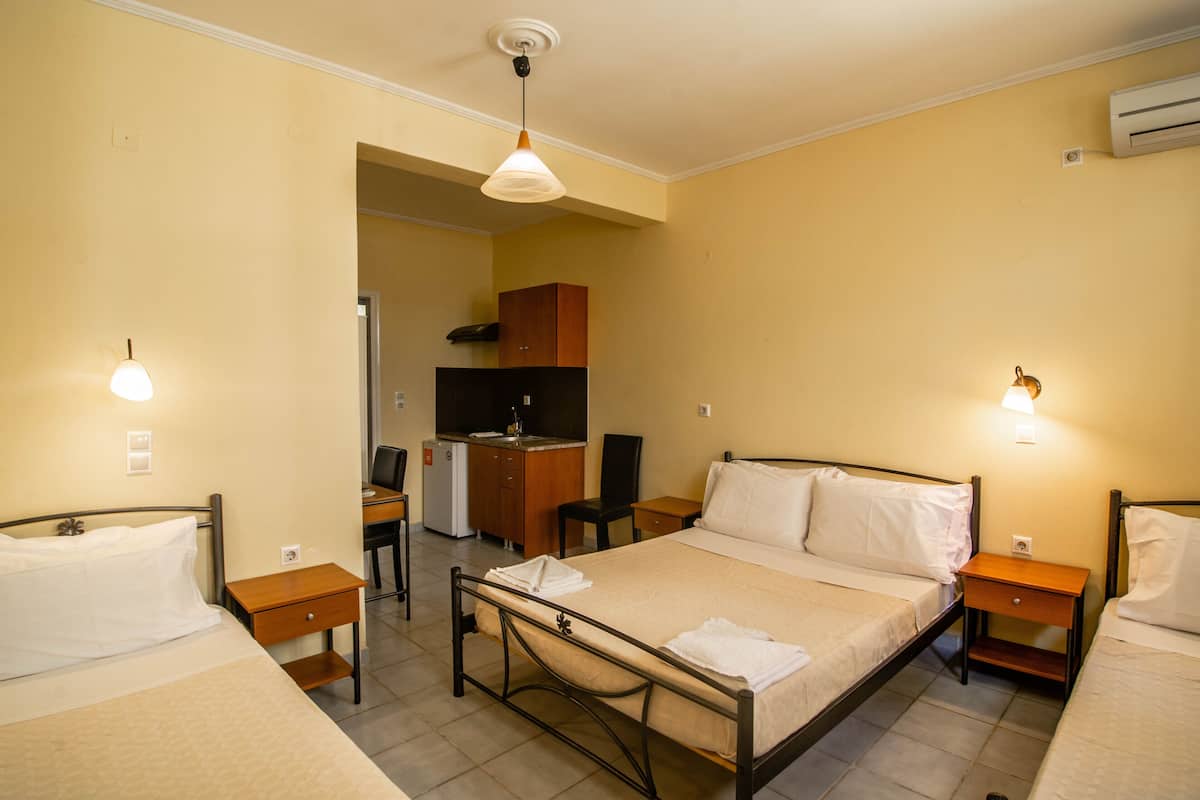 A hotel room with two single beds, a desk, a chair, a small kitchenette, and a bathroom.