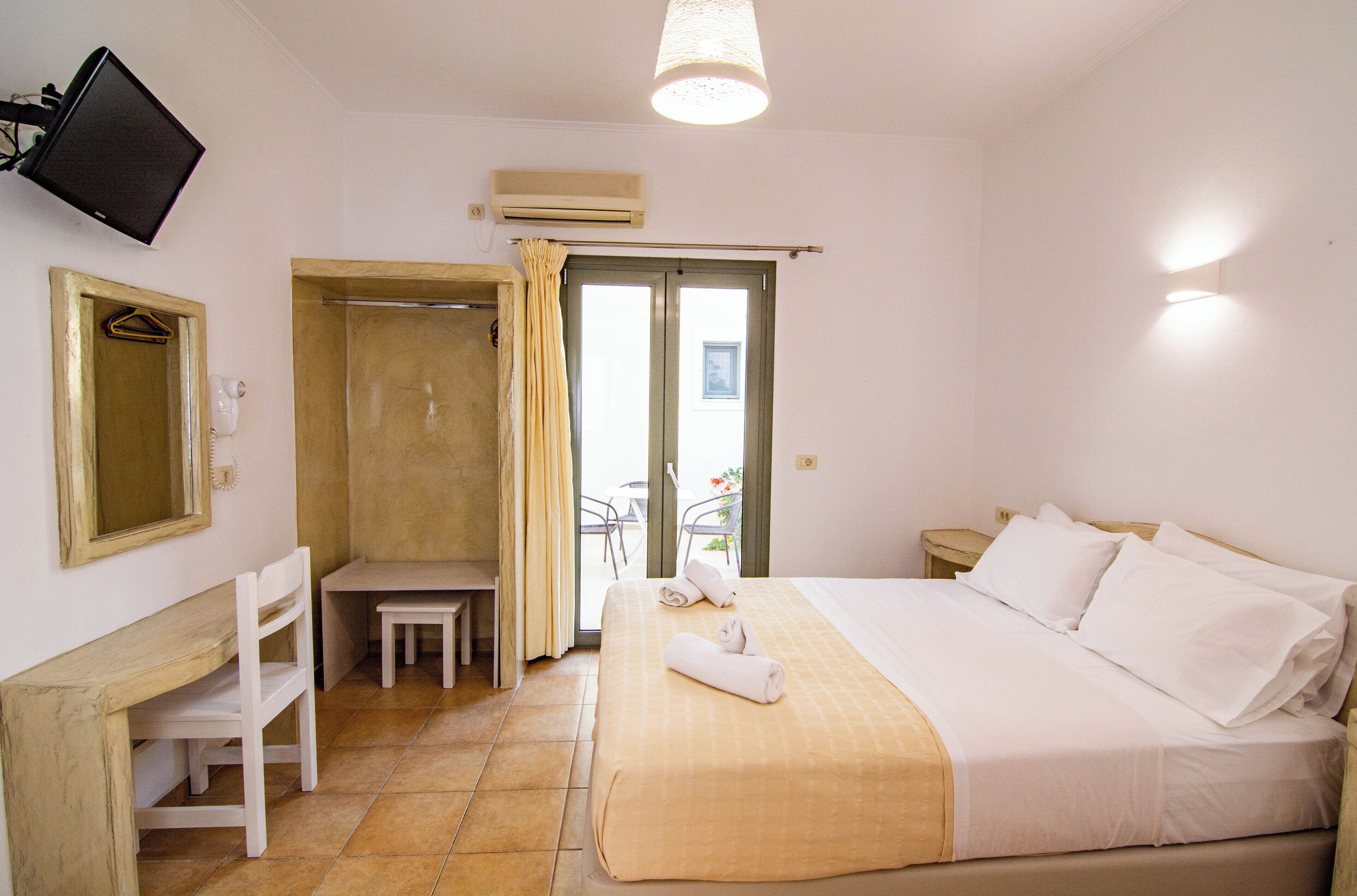 A hotel room with a bed, a desk, a chair, a TV, and a bathroom with a shower and a toilet.