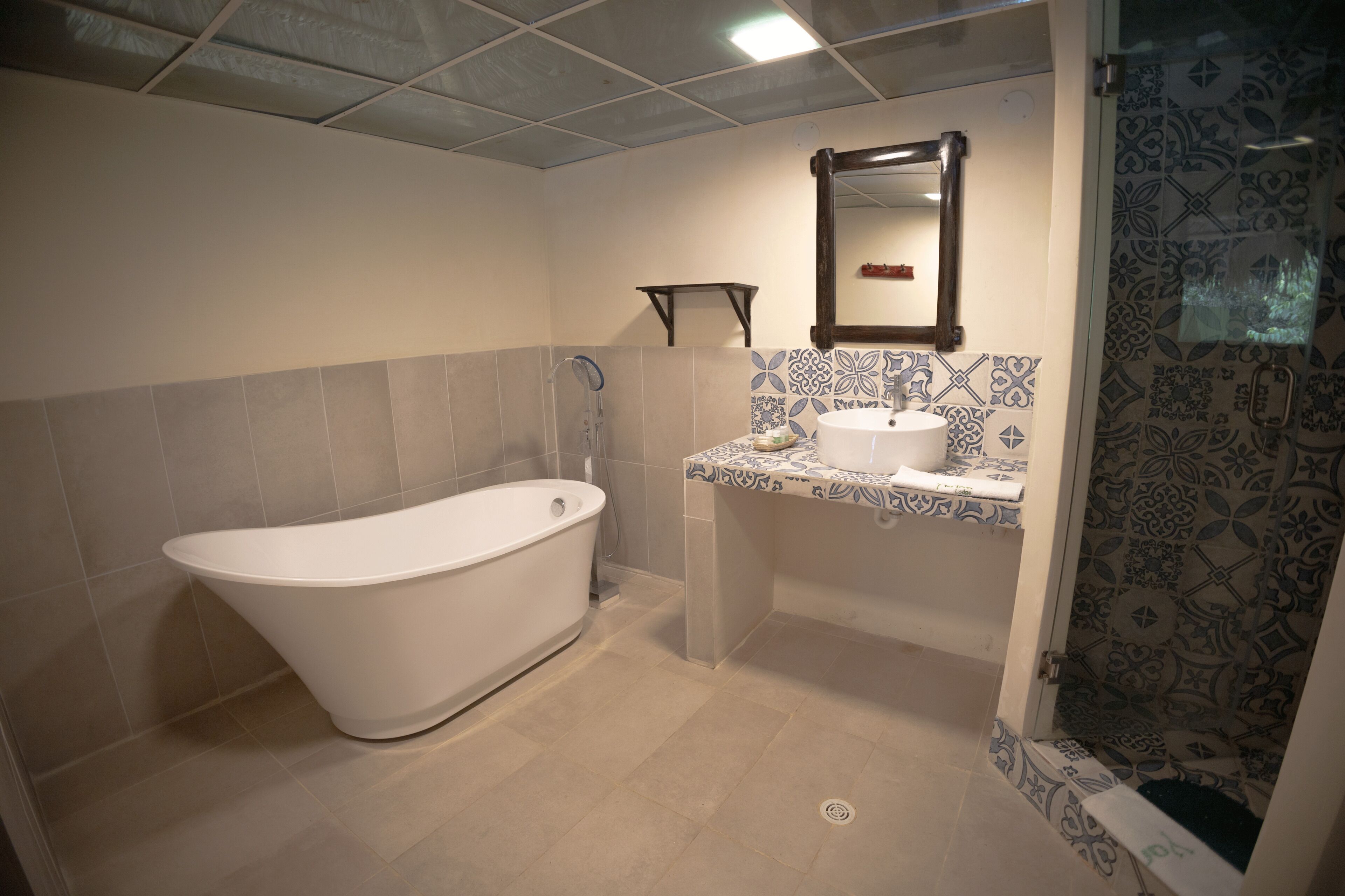 Un baño con una bañera independiente, un lavamanos con espejo y azulejos estampados en las paredes.