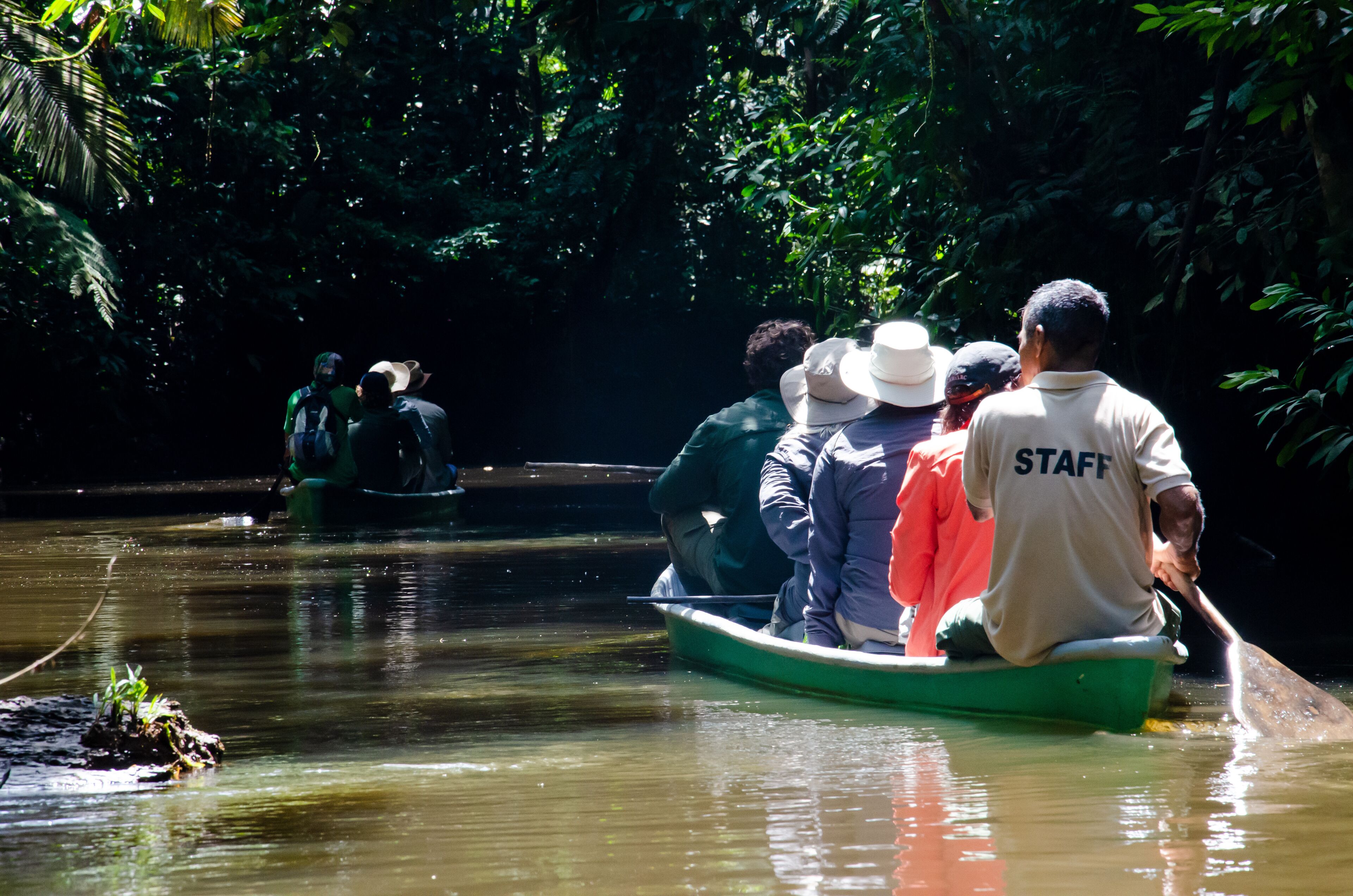 A group of people in a green boat on a calm river surrounded by dense foliage.