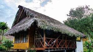 A rustic wooden house with a thatched roof, a wooden porch, and a garden with various plants and flowers.