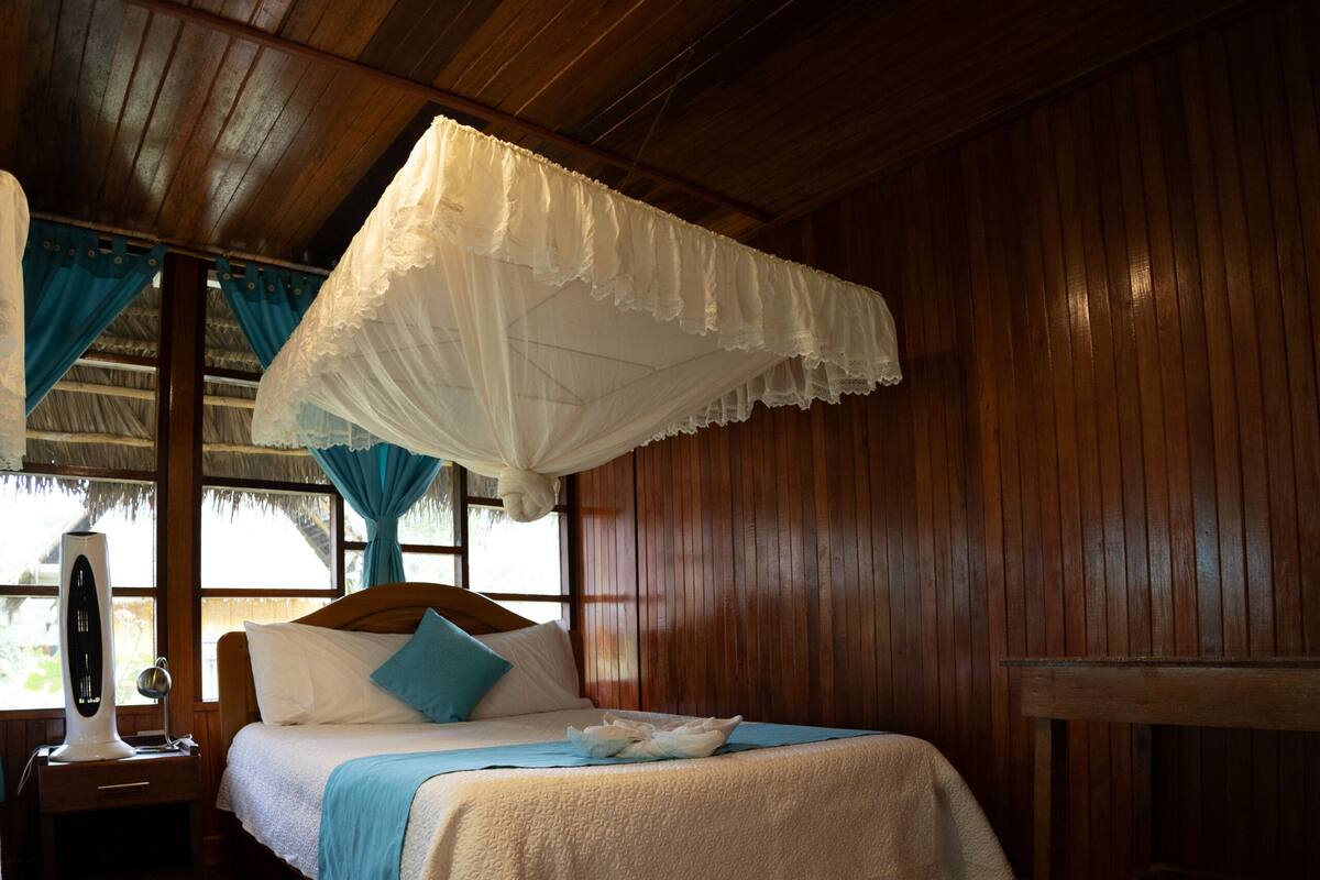 Una habitación de madera con una cama, una mesita de noche, una mesa y un dosel.