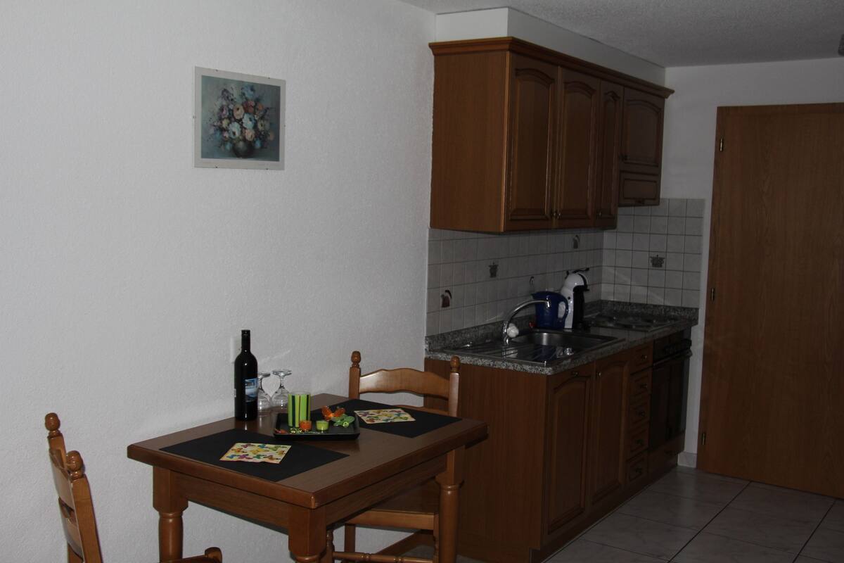 Una pequeña cocina con armarios de madera, una encimera y una mesa de comedor con sillas.