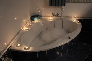 A bathtub with multiple candles, a blue basket, and a showerhead.