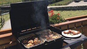 An outdoor grill with meat on a balcony overlooking a mountainous landscape. - Apartments Arcadia (Saas Grund)