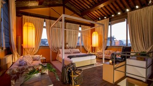 A four-poster bed with a canopy, a sofa, a desk with a lamp, and a view of the city through large windows. - Torre Mannelli Suites (Florence)