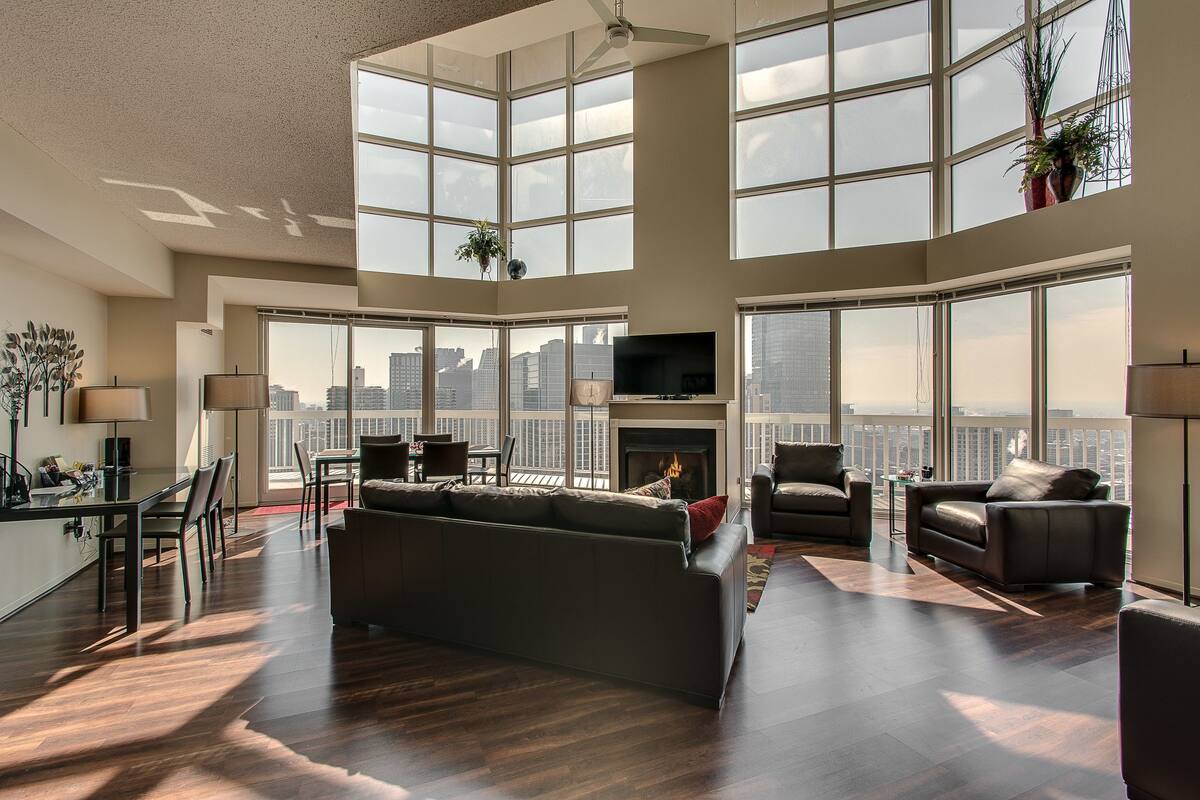 A spacious living room with a large window, a fireplace, and a city view.