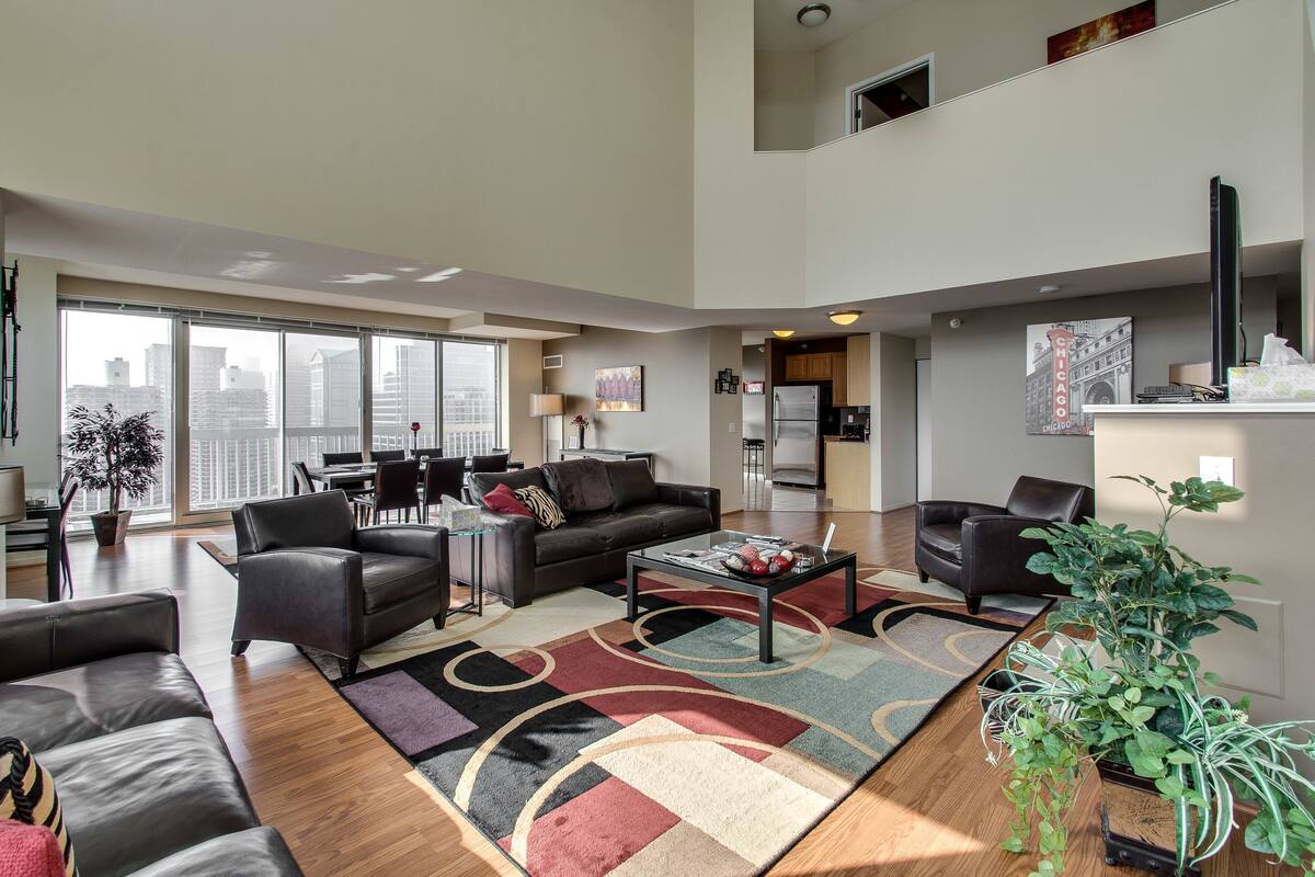 A spacious living area with a large window, a black leather sofa, a coffee table, and a potted plant.