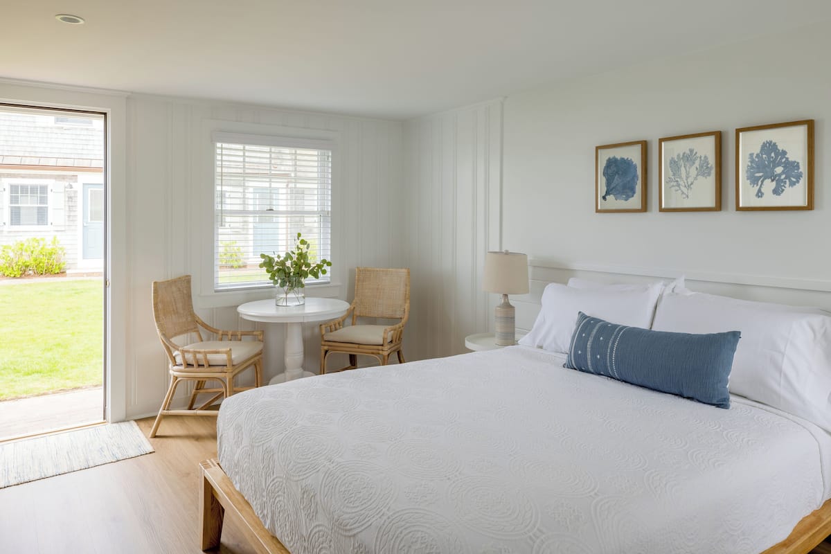 A bedroom with a large bed, two chairs, a small table with a plant, and three framed pictures on the wall.