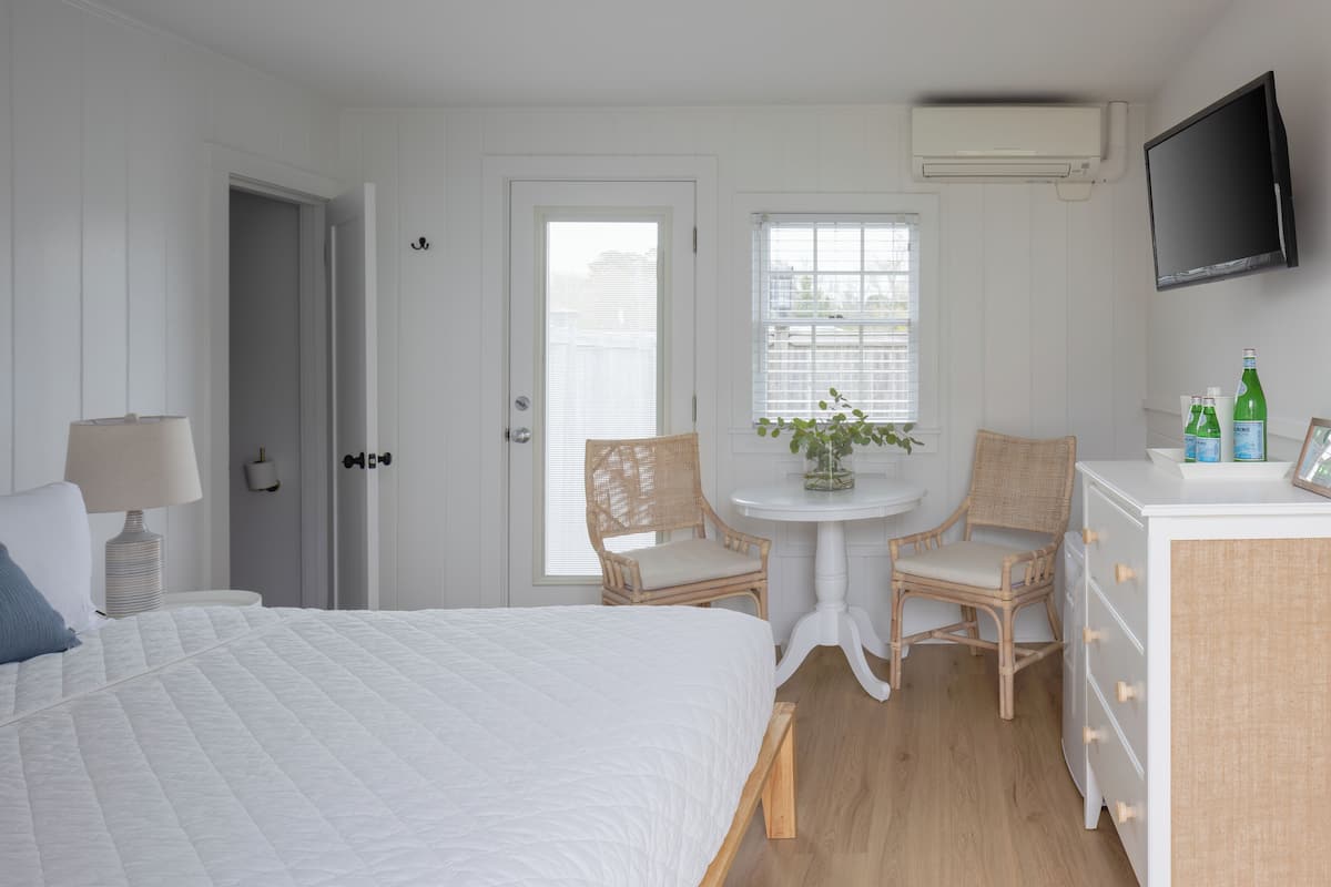 A bedroom with a bed, a desk, two chairs, a TV, and a window.