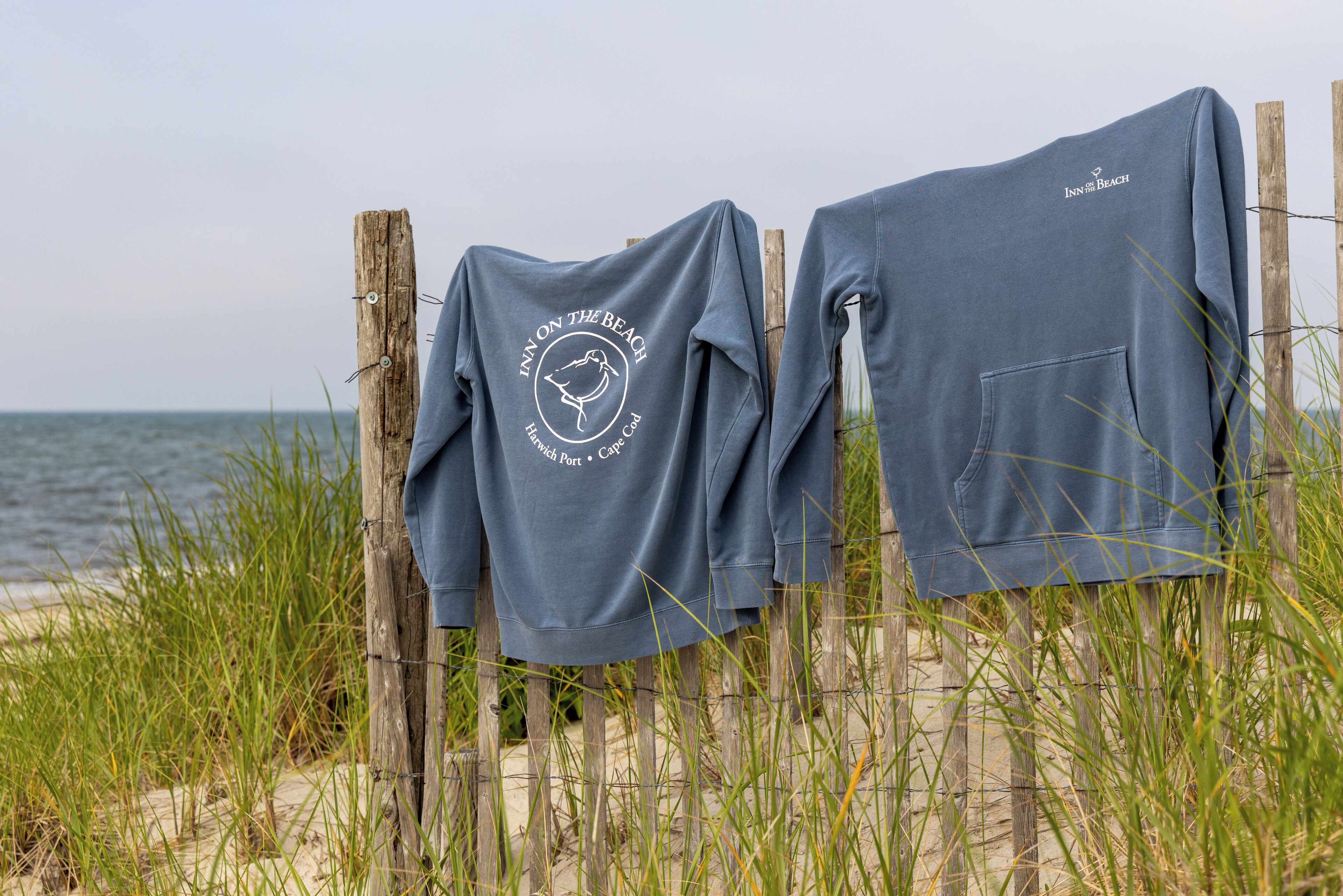 Deux pulls de sport gris sont suspendus à une clôture en bois, sur une plage.