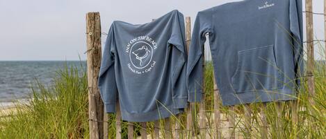 Deux pulls de sport gris sont suspendus à une clôture en bois, sur une plage.