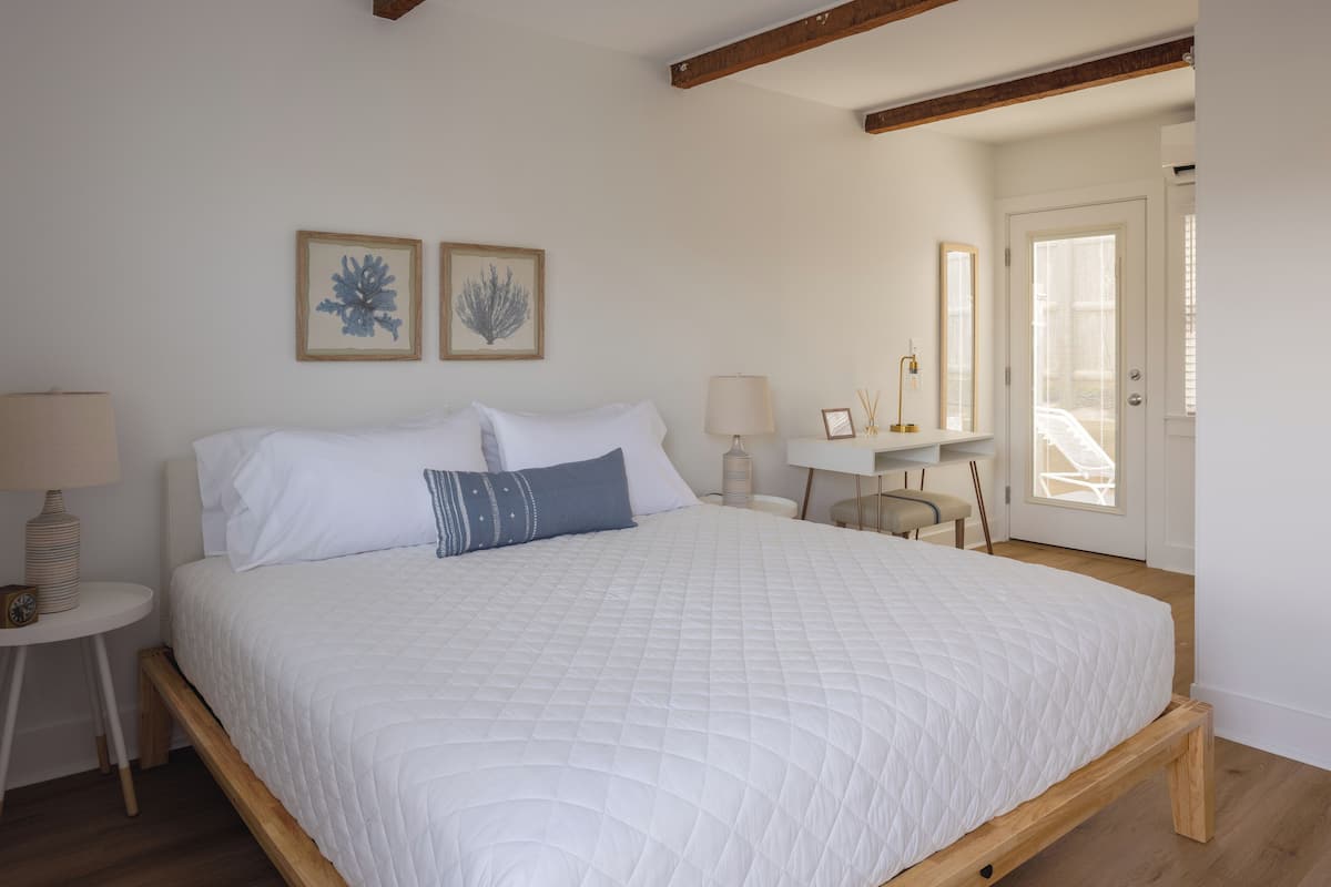 A bedroom with a large bed, a bedside table with a lamp, and a small table with a clock.