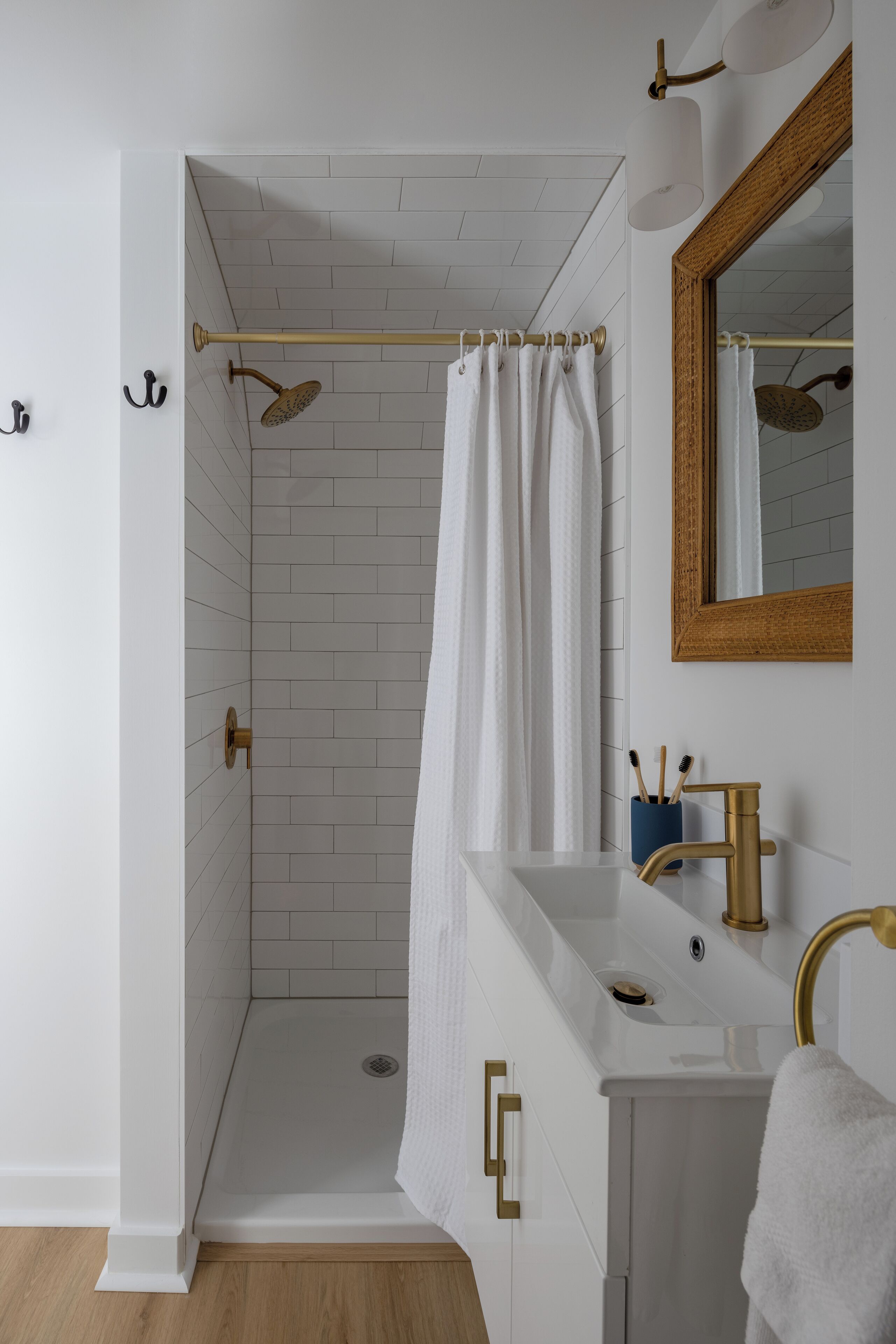 A modern bathroom with a walk-in shower, white tiled walls, a wooden-framed mirror, and a white sink with gold fixtures.