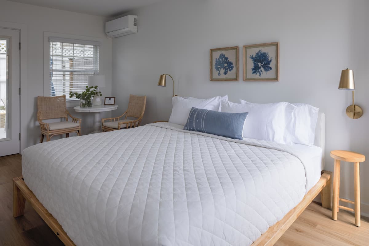 A bedroom with a large bed, two chairs, a small table, and two wall-mounted lamps.