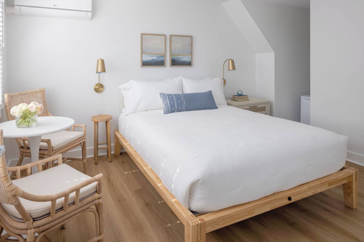 A neatly arranged bedroom with a wooden bed frame, a round table with chairs, and a small side table.