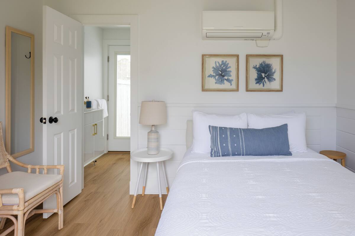A bedroom with a bed, a chair, a small table with a lamp, and two framed pictures on the wall.