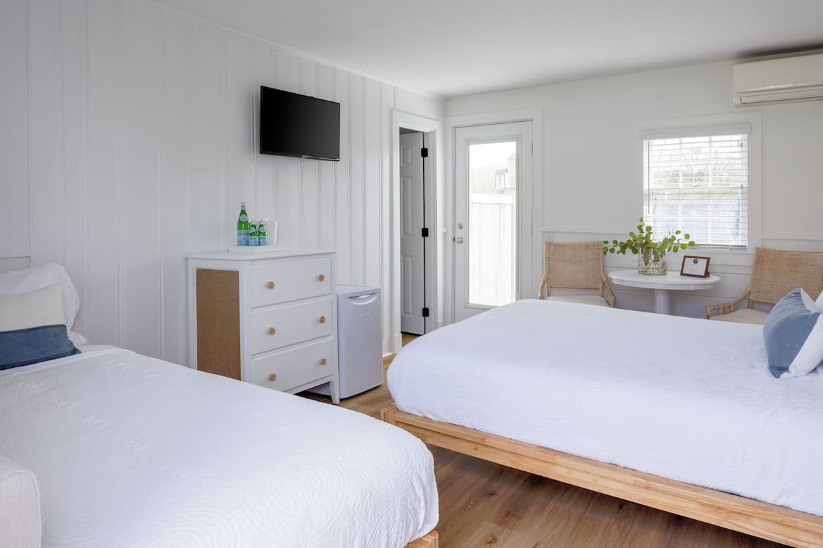 A hotel room with two beds, a TV, a small table with a vase, and a window with blinds.