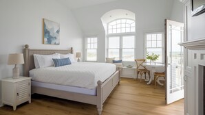 A bedroom with a large bed, a desk, and a chair, a window with a view, and a painting on the wall. - Inn on the Beach  (Harwich Port)