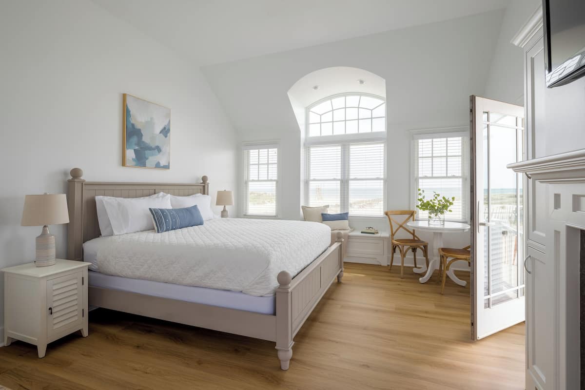 A bedroom with a large bed, a desk, and a chair, a window with a view, and a painting on the wall.