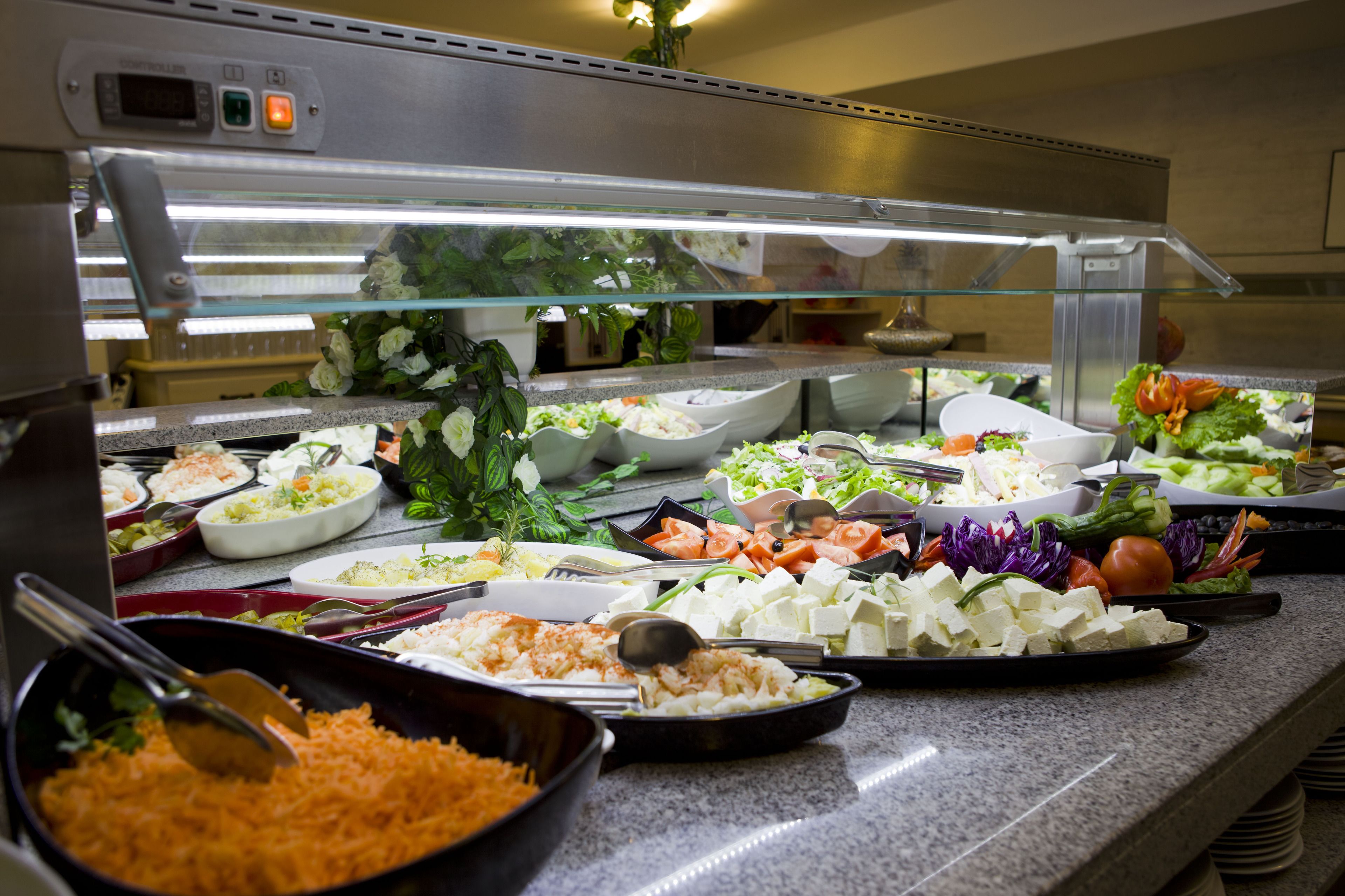 En buffet med flere forskellige retter, heriblandt salater, oste og tilberedte grøntsager.